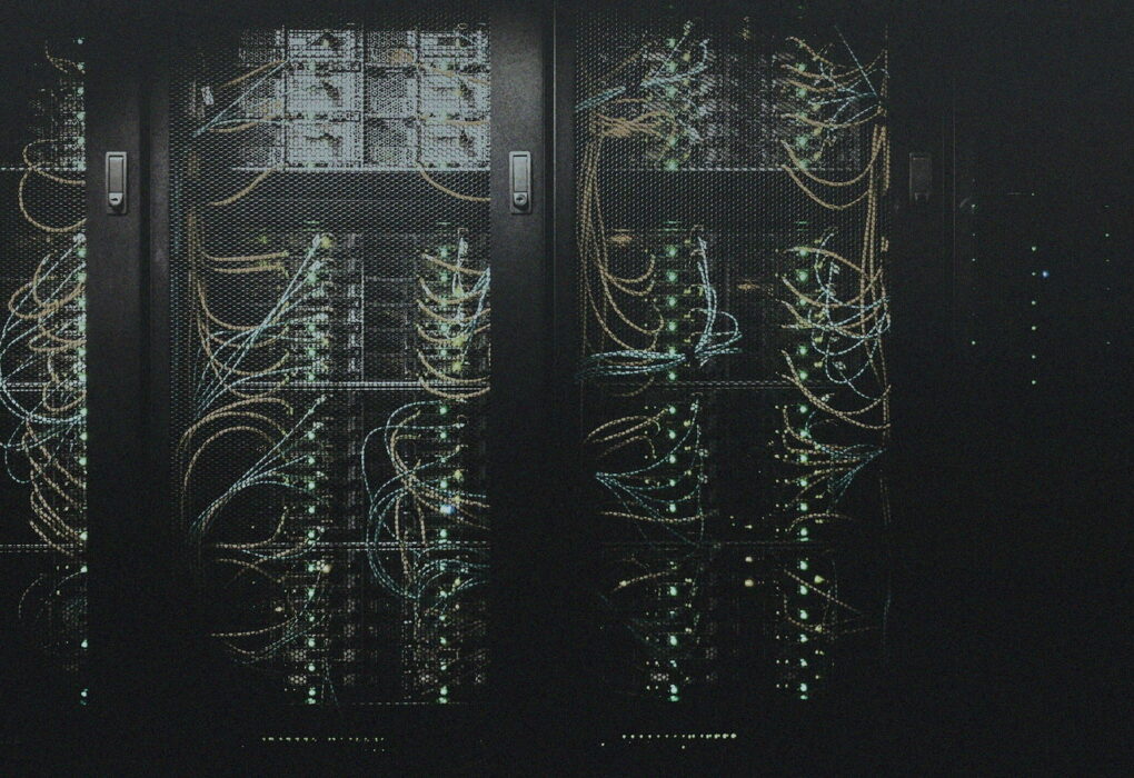 Dim server racks behind mesh doors with status lights and cables, no people or brand logos — always-on compute mood for a desk AI box