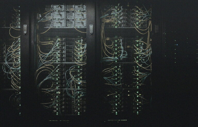 Dim server racks behind mesh doors with status lights and cables, no people or brand logos — always-on compute mood for a desk AI box