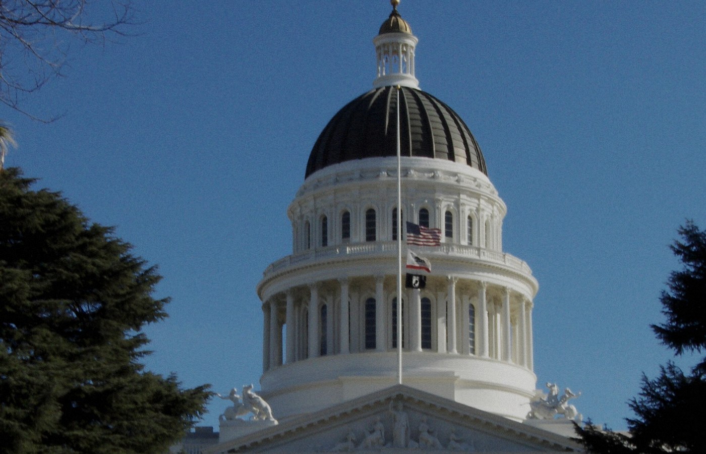 Face-free Wikimedia Commons photograph of the California State Capitol dome and flags in Sacramento — hero for California lawmakers demanding criminal AI penalties and emergency guardrails September 2026