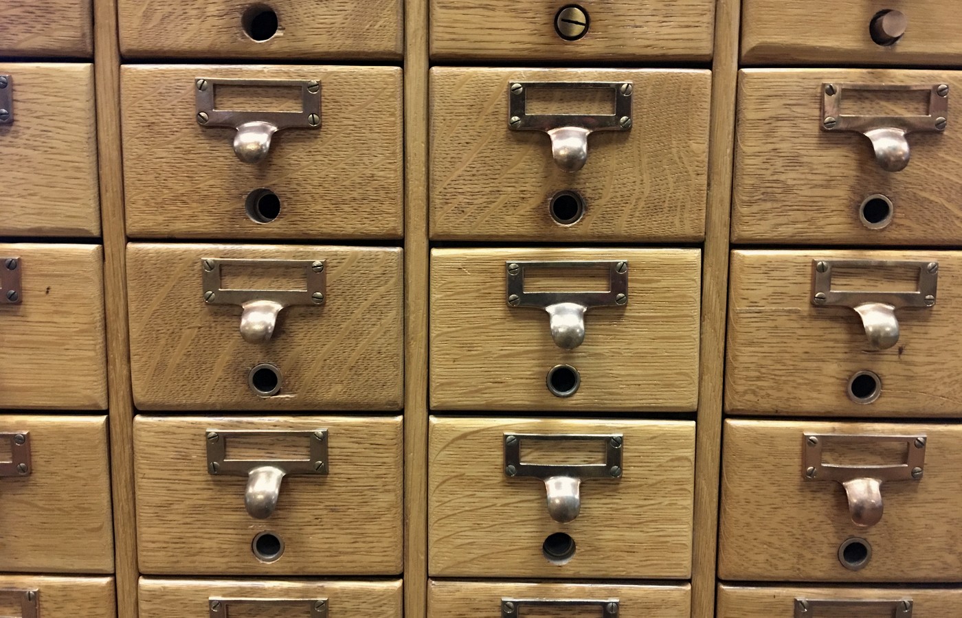 Close-up of wooden library card catalog drawers with blank brass label holders