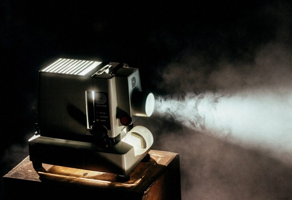 Vintage Dukane filmstrip projector casting a bright beam in darkness, face-free still for Google DeepMind Gemini agentic video understanding