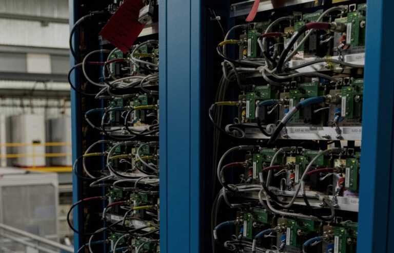 Close-up of two blue industrial server racks packed with green circuit modules and dense multi-color cabling in a face-free facility still for iPronics OCS coverage