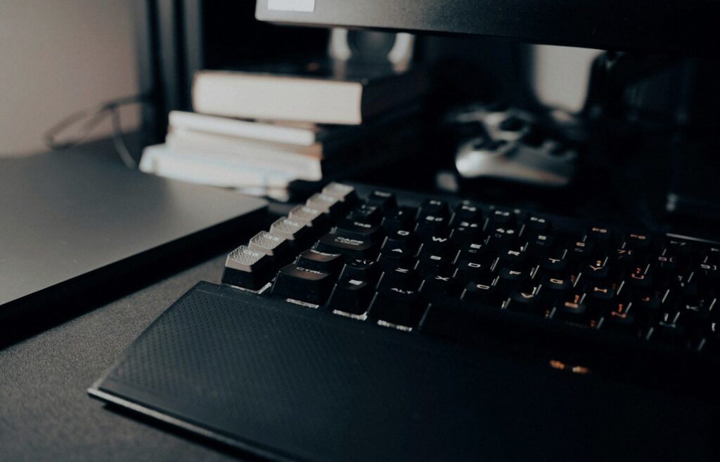 Face-free close-up of a black mechanical keyboard on a dark desk with orange key lighting and notebooks in soft focus — coding desk still for Cognition Series E Devin coverage