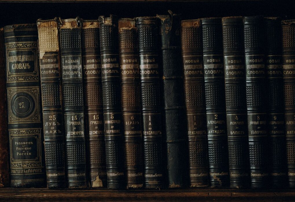 Face-free Unsplash close-up of antique leather-bound encyclopedic books on a dark shelf — hero for OpenAI Congress antitrust ask on AI industry slowdown legality September 2026