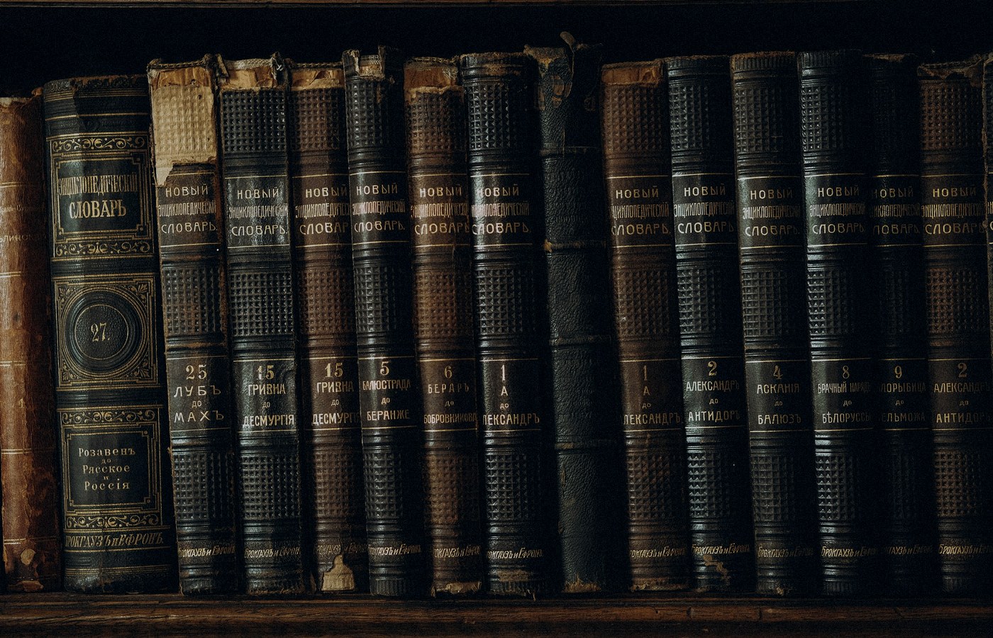 Face-free Unsplash close-up of antique leather-bound encyclopedic books on a dark shelf — hero for OpenAI Congress antitrust ask on AI industry slowdown legality September 2026