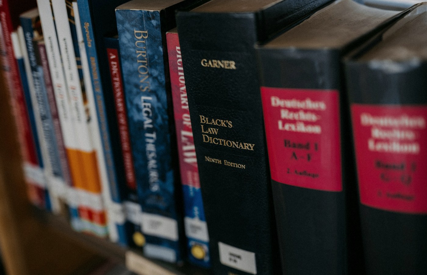 Face-free row of law books lined up on a wooden shelf — legal research metaphor hero still for Harvey legal AI $550M round at $15.5B valuation and Guardrails AI acquisition Sep 9 2026