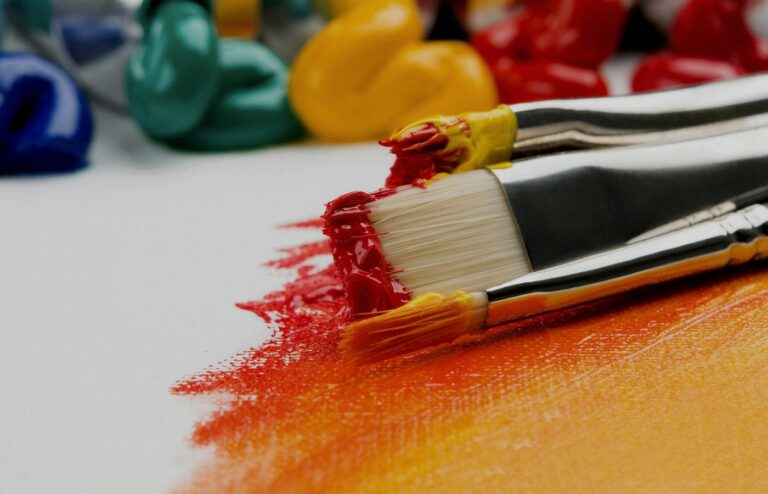 Face-free close-up of silver paint brushes with red and yellow paint on a white canvas — creative still for Microsoft MAI-Image-2.6 Foundry public preview coverage