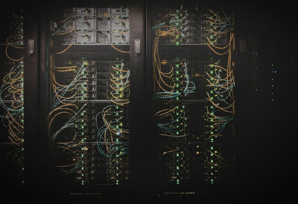 Face-free server racks with illuminated blue green and orange network cables behind mesh panels — related home-LAN multi-node compute still for NVIDIA PAIR Personal AI Router local inference coverage