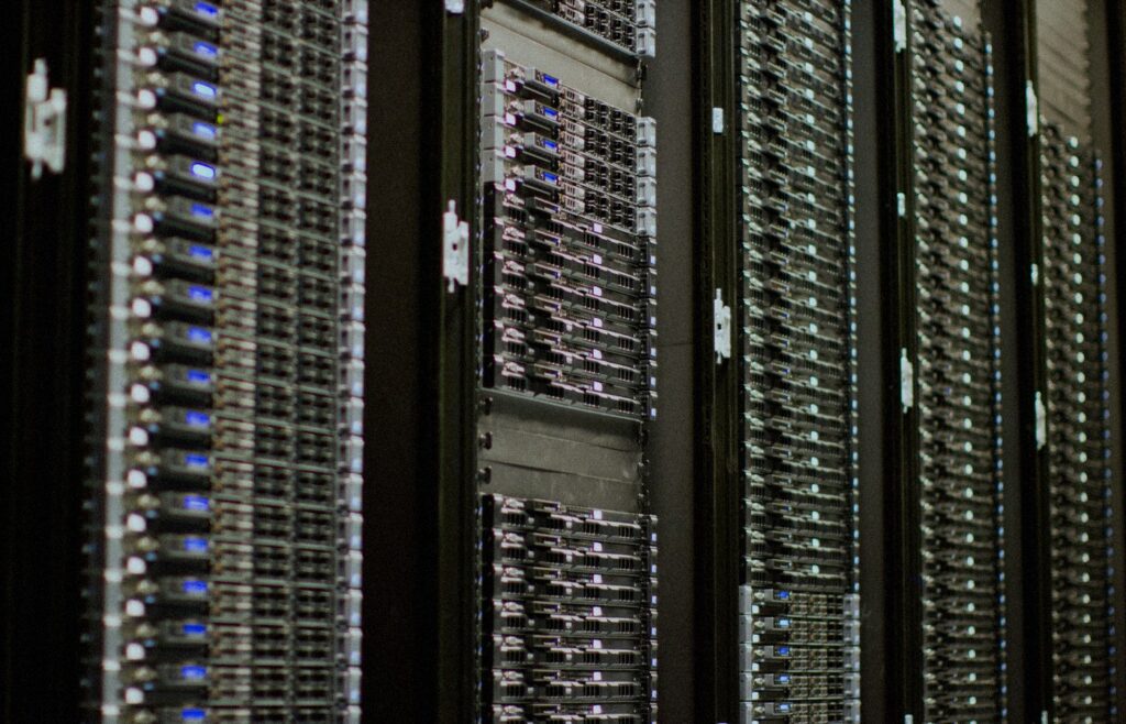 Close-up of face-free data-center server racks with rows of blue status LEDs receding into soft focus — AI cloud compute still for Nscale × Figure coverage