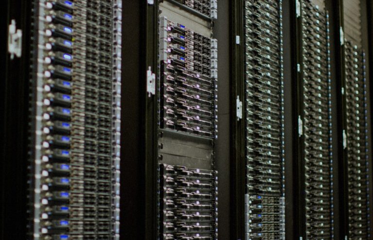 Close-up of face-free data-center server racks with rows of blue status LEDs receding into soft focus — AI cloud compute still for Nscale × Figure coverage