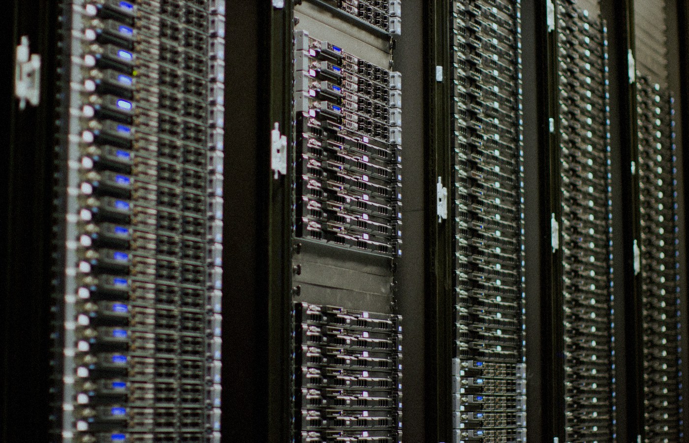 Close-up of face-free data-center server racks with rows of blue status LEDs receding into soft focus — AI cloud compute still for Nscale × Figure coverage