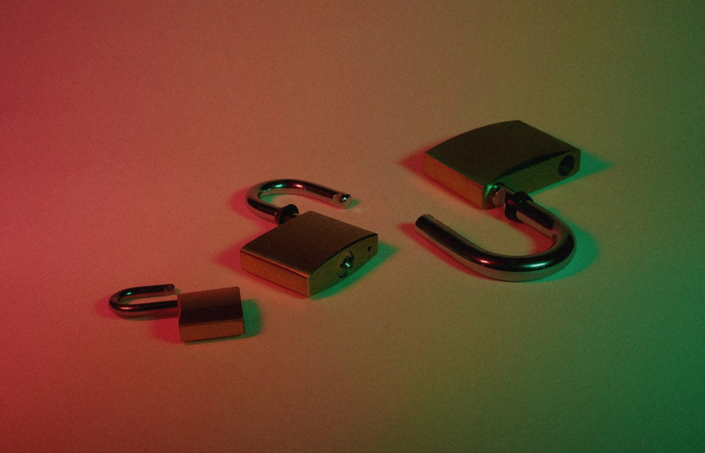 Three open brass padlocks on a surface under red-to-green dramatic lighting, face-free still for OpenAI Astra Critical cybersecurity capability