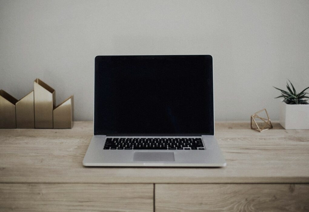 Face-free Unsplash photograph of a closed silver laptop on a brown wooden desk with a small plant — related still for Apple Siri AI / iOS 27 family September 2026