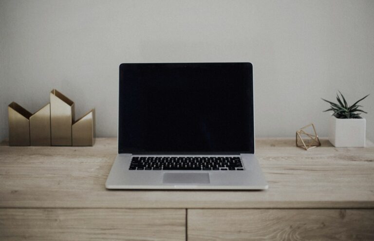 Face-free Unsplash photograph of a closed silver laptop on a brown wooden desk with a small plant — related still for Apple Siri AI / iOS 27 family September 2026