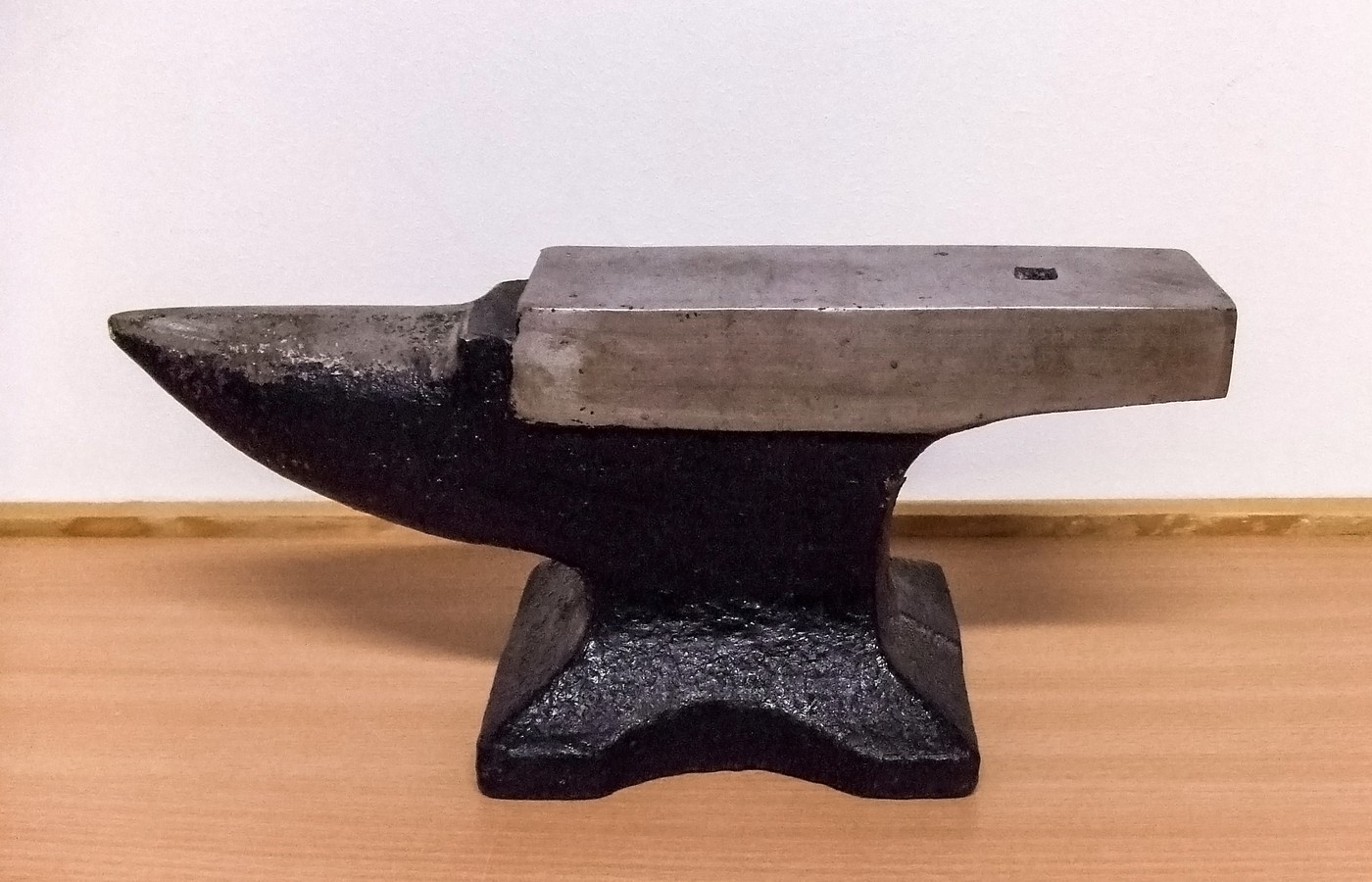 A small black cast bench anvil with a polished steel face on a light wooden shelf against a white wall