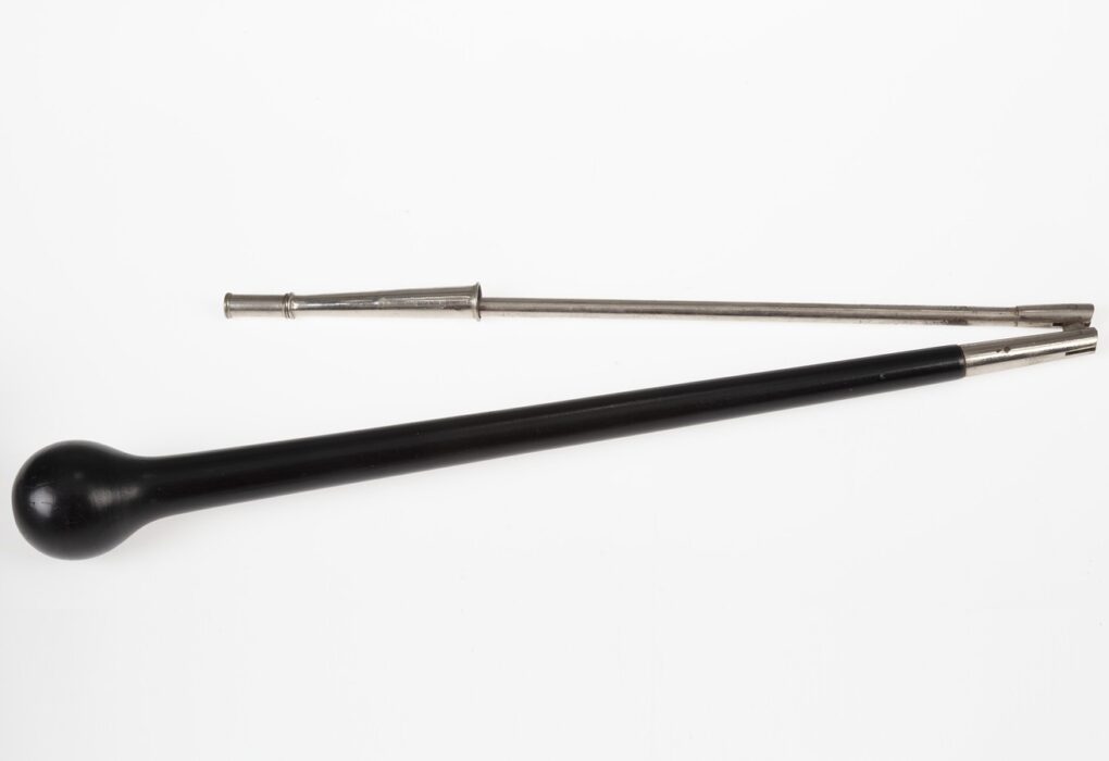 A black ebony drum major baton with a round ball head lying beside its separate silver metal shaft on a plain white backdrop