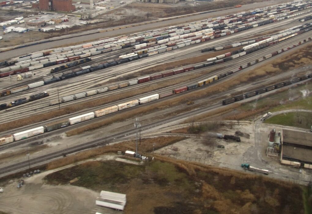 Aerial view of a large rail classification yard with dozens of parallel tracks full of freight cars running toward the horizon, with no people in frame