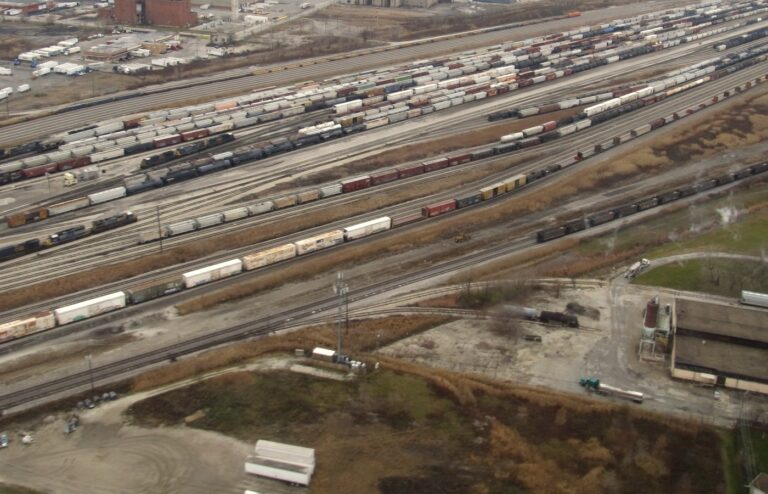 Aerial view of a large rail classification yard with dozens of parallel tracks full of freight cars running toward the horizon, with no people in frame