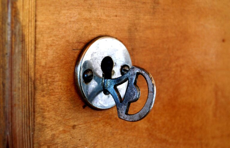 An old iron key left in a round, worn metal escutcheon on a warm wooden door, with a vertical door frame on the left and no people in frame