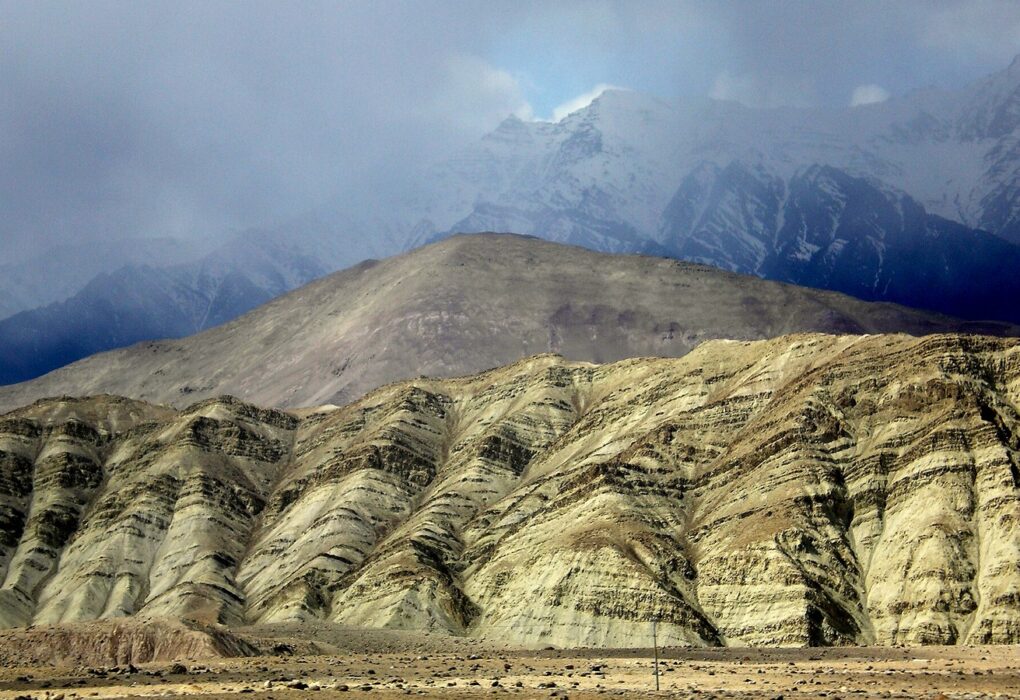 Tilted sedimentary rock layers in an arid mountain landscape under cloud, with no people in frame