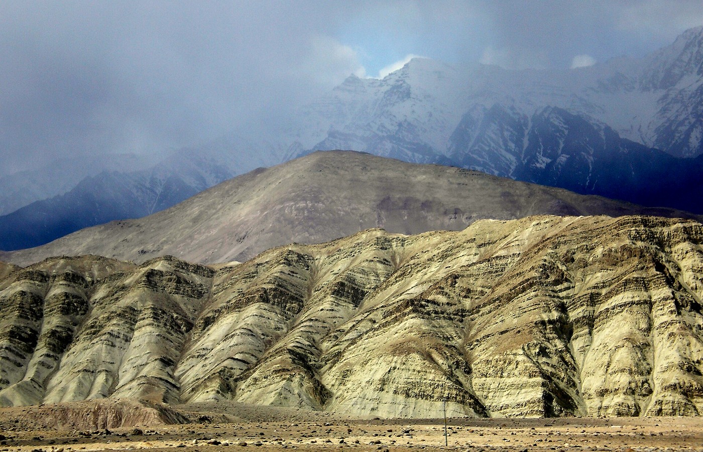 Tilted sedimentary rock layers in an arid mountain landscape under cloud, with no people in frame