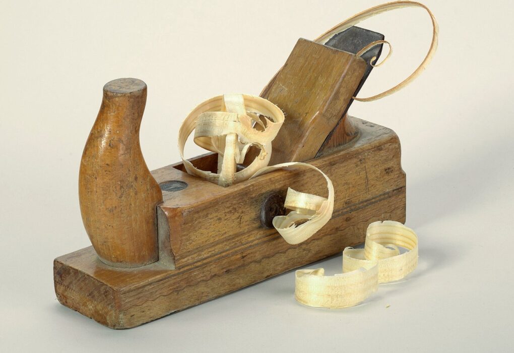 Wooden hand plane with curled wood shavings on a plain light background