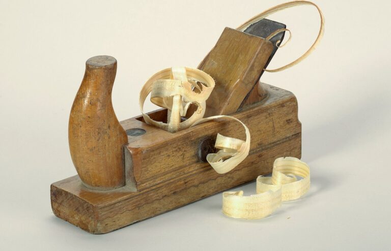 Wooden hand plane with curled wood shavings on a plain light background