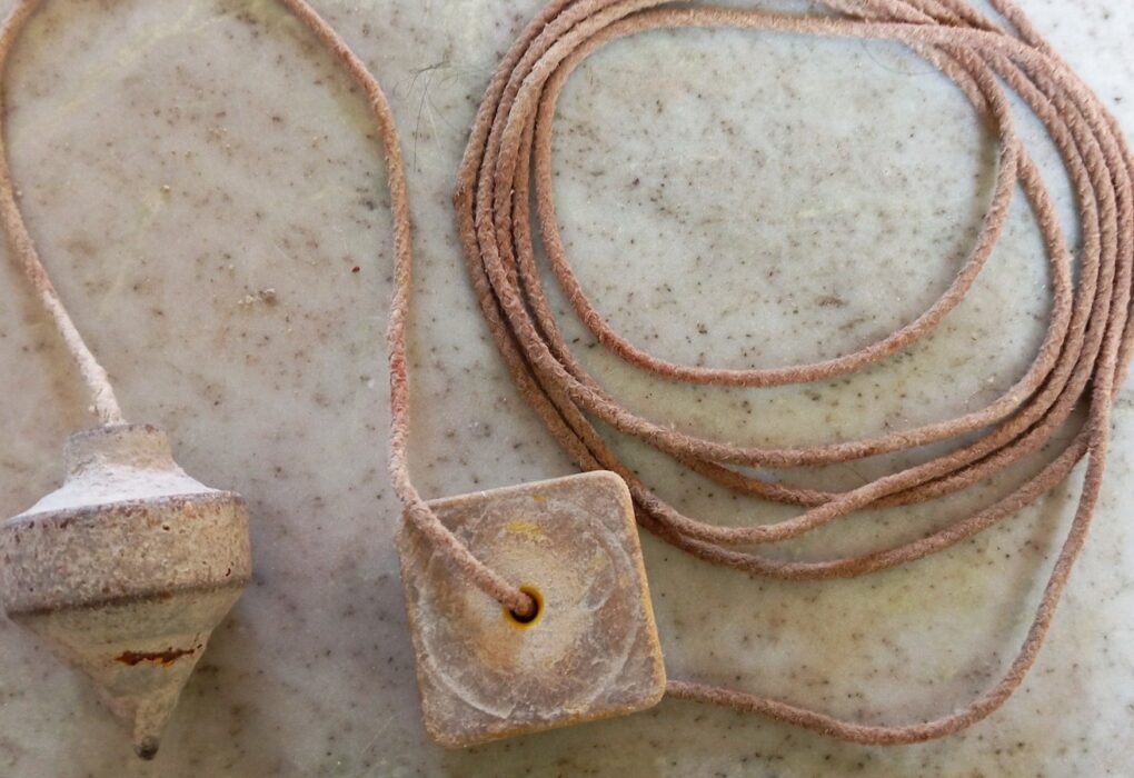 A worn metal plumb bob and its square wooden line block with a coiled cord, on a speckled marble surface