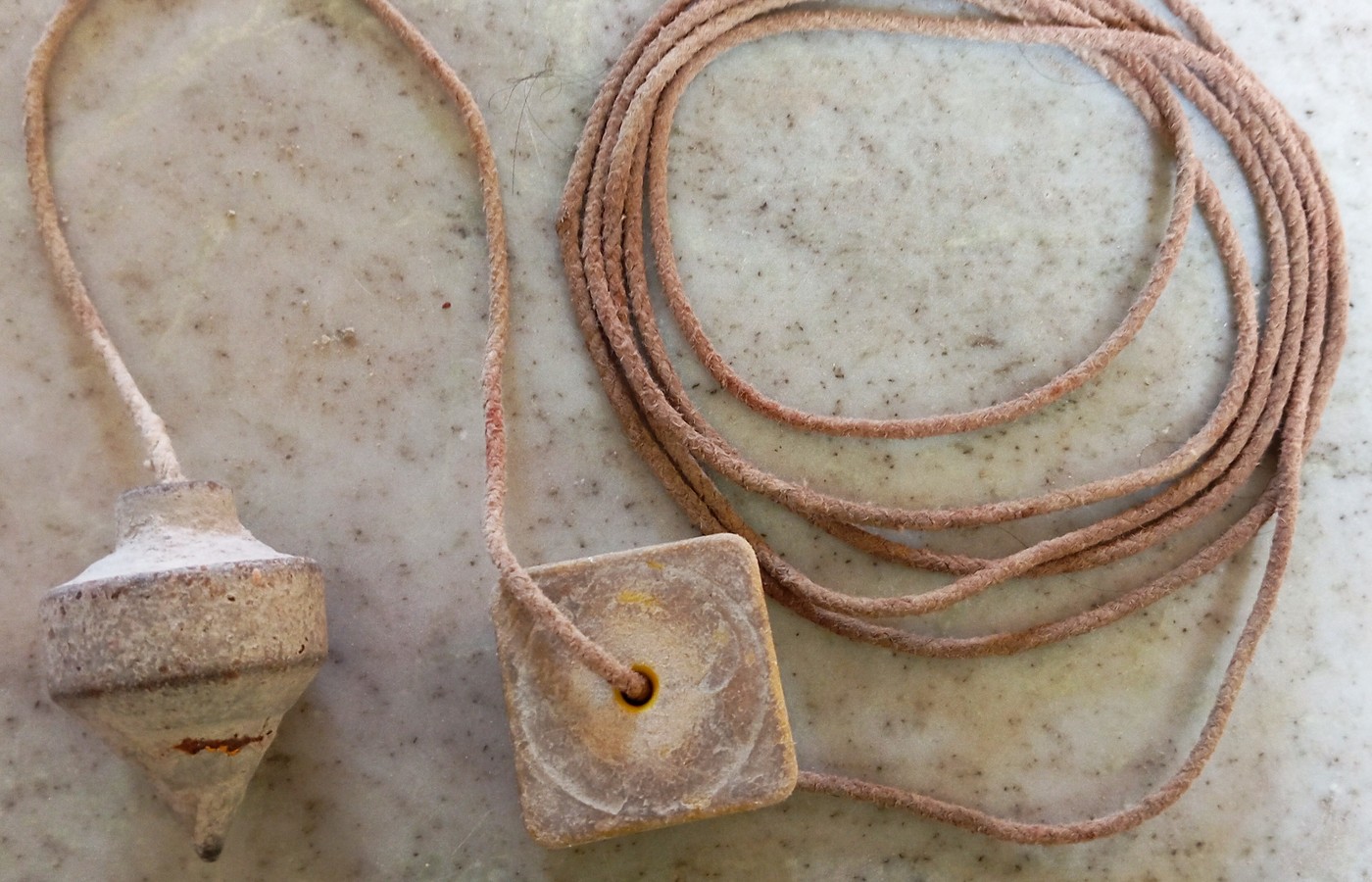 A worn metal plumb bob and its square wooden line block with a coiled cord, on a speckled marble surface