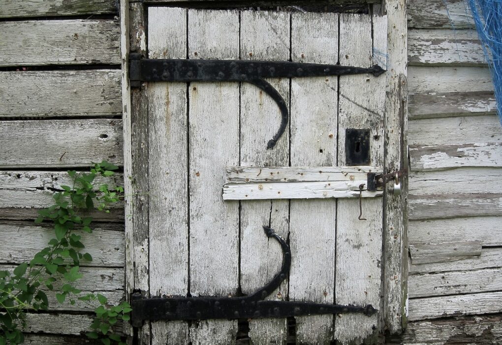 Face-free photo of a weathered wooden door with iron strap hinges and a closed latch