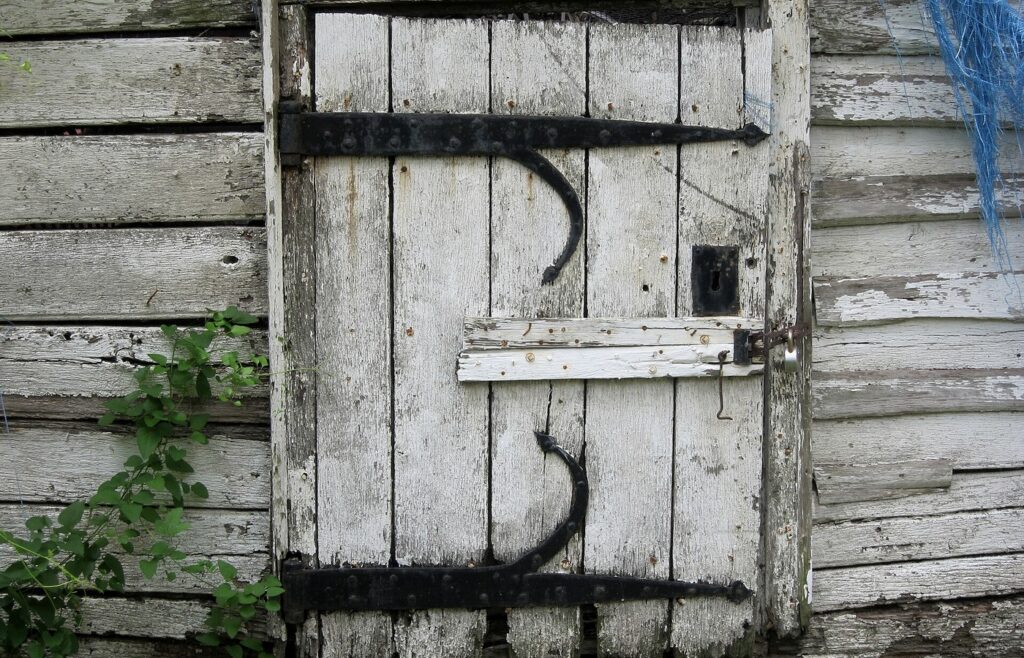 Face-free photo of a weathered wooden door with iron strap hinges and a closed latch