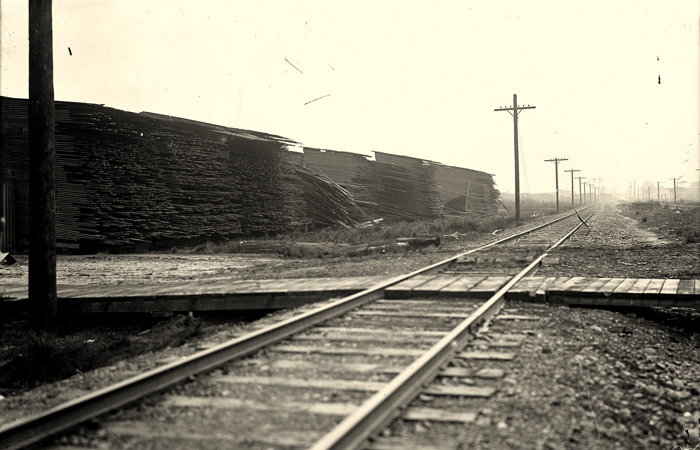 Stacked fir planks beside a rail line, with utility poles and no people in frame