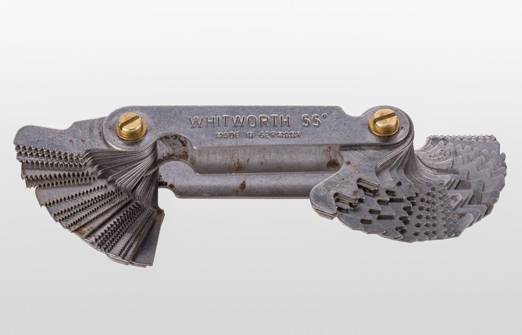 A steel thread pitch gauge, a folded fan of metal blades with different tooth patterns, on a plain light grey background
