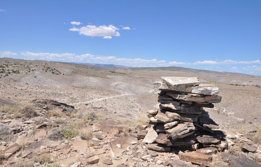 A stacked-stone trail cairn on a dry Utah desert ridge under a blue sky