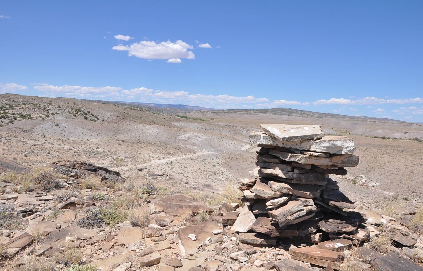 A stacked-stone trail cairn on a dry Utah desert ridge under a blue sky